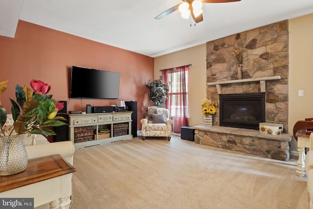 carpeted living room featuring a stone fireplace and ceiling fan