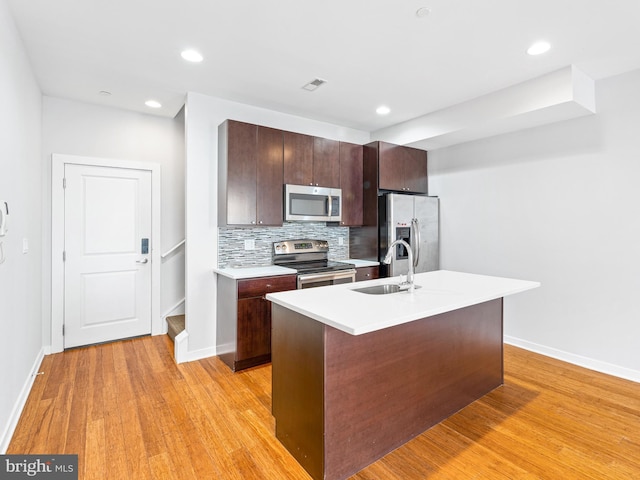 kitchen with sink, decorative backsplash, a kitchen island with sink, stainless steel appliances, and light wood-type flooring