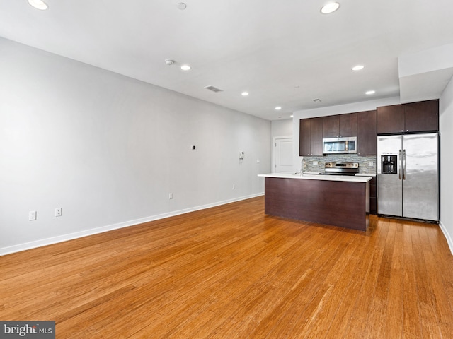 kitchen featuring dark brown cabinetry, stainless steel appliances, light wood-type flooring, and backsplash