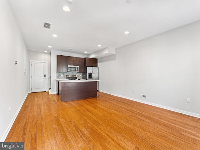 kitchen with backsplash, dark brown cabinets, stainless steel appliances, a kitchen island, and light wood-type flooring