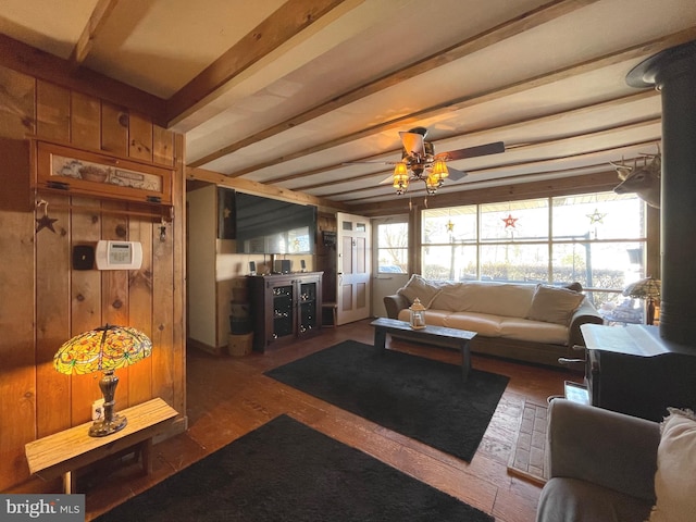 living room with beam ceiling, dark wood-type flooring, ceiling fan, and wood walls