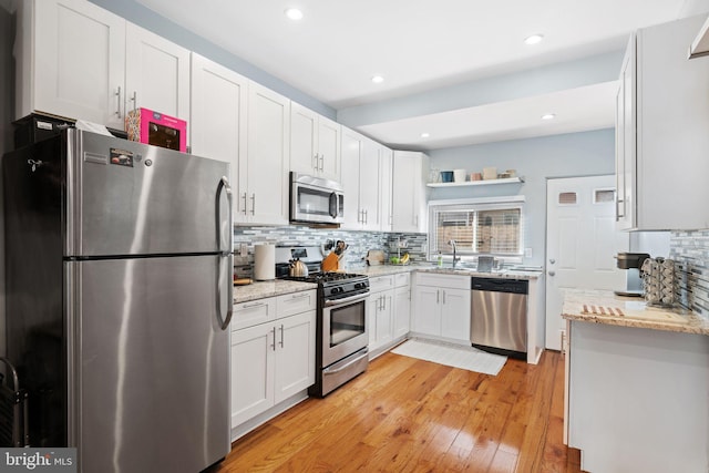 kitchen featuring white cabinetry, light wood-type flooring, stainless steel appliances, and decorative backsplash