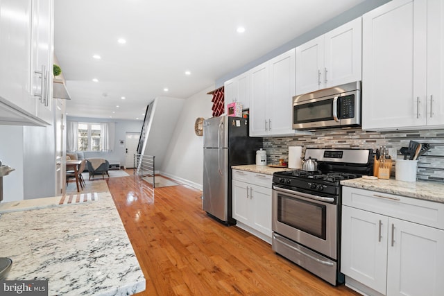 kitchen featuring light stone counters, light wood-type flooring, white cabinetry, stainless steel appliances, and decorative backsplash