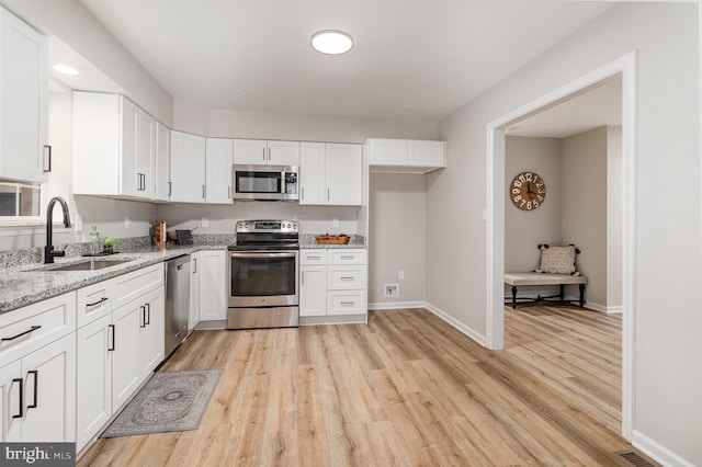 kitchen with appliances with stainless steel finishes, white cabinetry, sink, light stone counters, and light hardwood / wood-style flooring