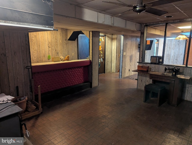 bar featuring a drop ceiling, ceiling fan, and wood walls