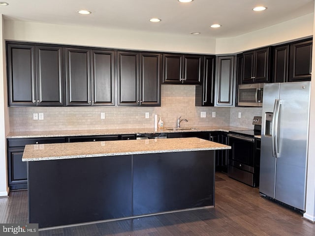 kitchen with a kitchen island, appliances with stainless steel finishes, dark hardwood / wood-style floors, sink, and light stone countertops