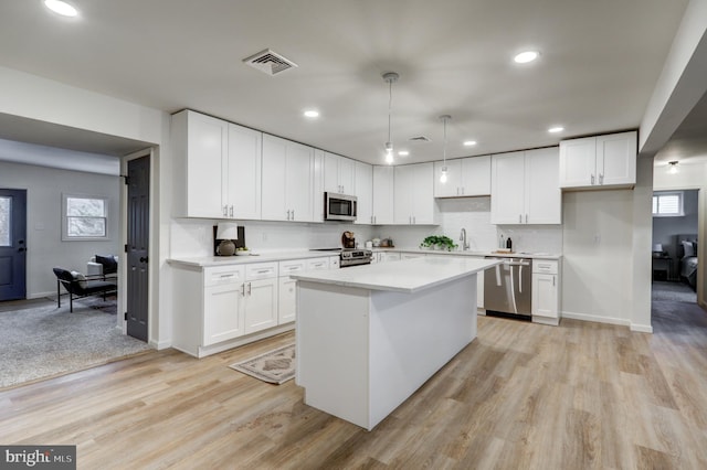 kitchen featuring appliances with stainless steel finishes, hanging light fixtures, and white cabinets