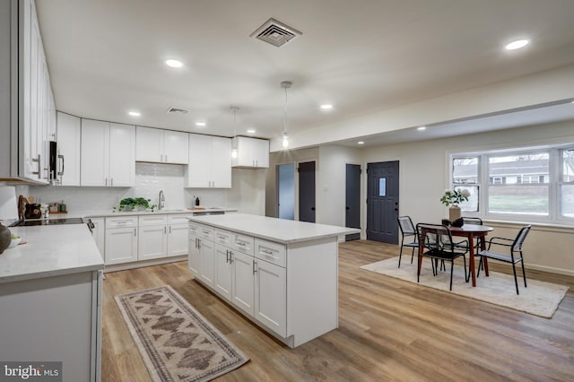 kitchen with white cabinetry, hanging light fixtures, a kitchen island, and light wood-type flooring