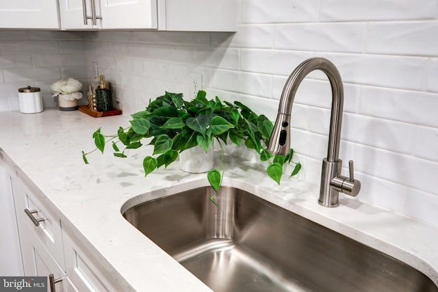 room details featuring tasteful backsplash, sink, light stone counters, and white cabinets