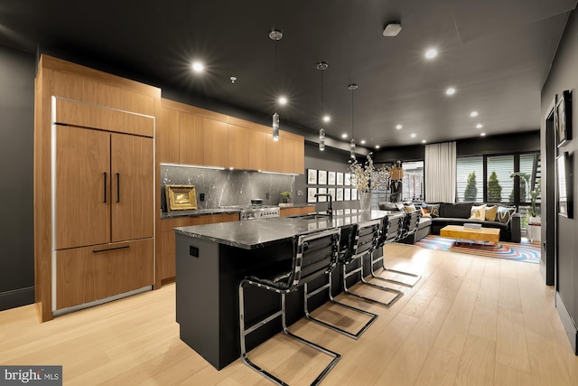 kitchen featuring sink, a breakfast bar area, dark stone countertops, a spacious island, and paneled refrigerator