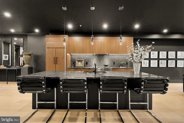 kitchen with sink, a breakfast bar area, hanging light fixtures, dark stone counters, and a large island