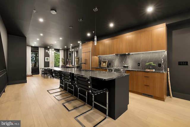 kitchen featuring decorative light fixtures, dark stone countertops, a kitchen breakfast bar, a large island, and light hardwood / wood-style floors