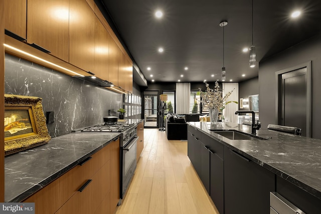 kitchen featuring sink, light wood-type flooring, stainless steel stove, pendant lighting, and dark stone counters