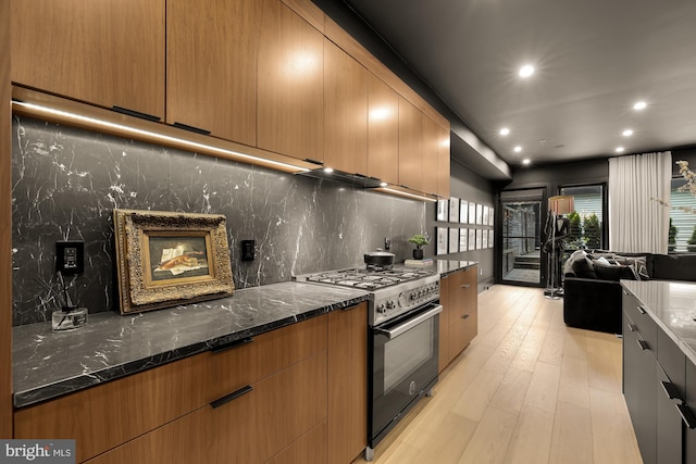 kitchen featuring dark stone countertops, backsplash, stainless steel range, and light hardwood / wood-style flooring