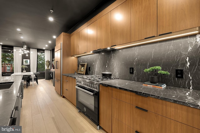 kitchen featuring pendant lighting, dark stone countertops, tasteful backsplash, range with gas stovetop, and light wood-type flooring