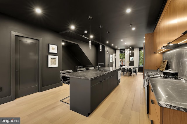 kitchen with sink, dark stone countertops, a breakfast bar area, light wood-type flooring, and a spacious island