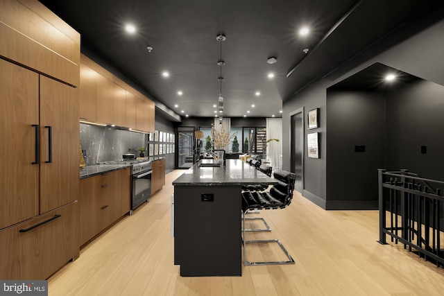 kitchen with a breakfast bar area, dark stone counters, a large island with sink, high end appliances, and light wood-type flooring