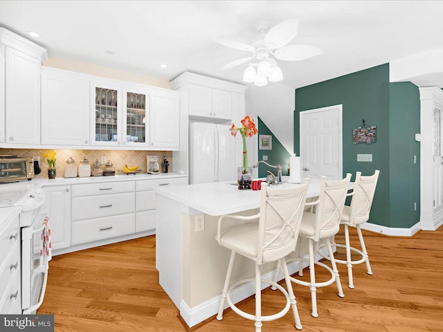 kitchen with white appliances, white cabinetry, a kitchen island with sink, and a breakfast bar