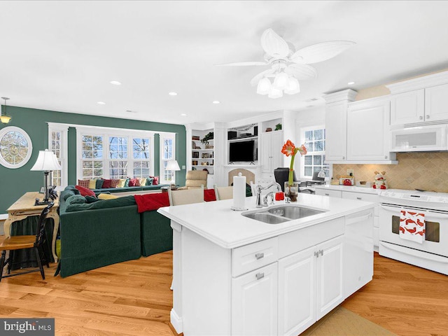 kitchen with white appliances, a center island with sink, sink, light wood-type flooring, and white cabinetry