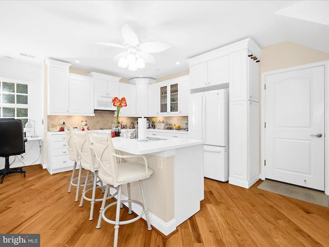 kitchen featuring an island with sink, white appliances, white cabinets, a kitchen bar, and decorative backsplash