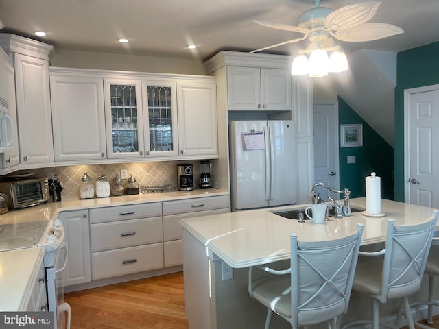 kitchen featuring white cabinetry, a kitchen island with sink, a breakfast bar, sink, and white appliances