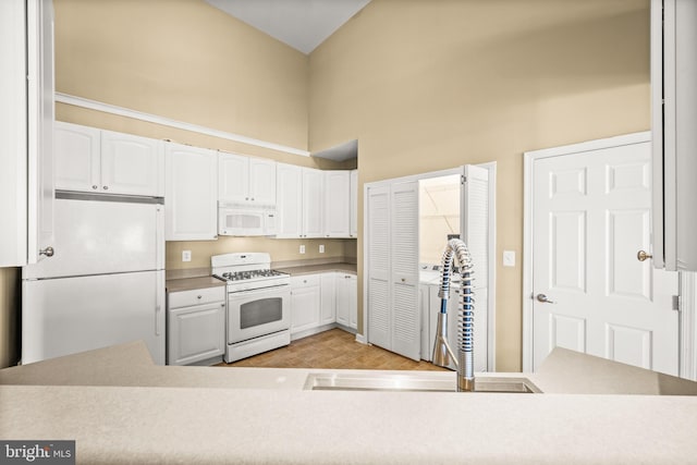 kitchen featuring white cabinetry, sink, white appliances, and a towering ceiling