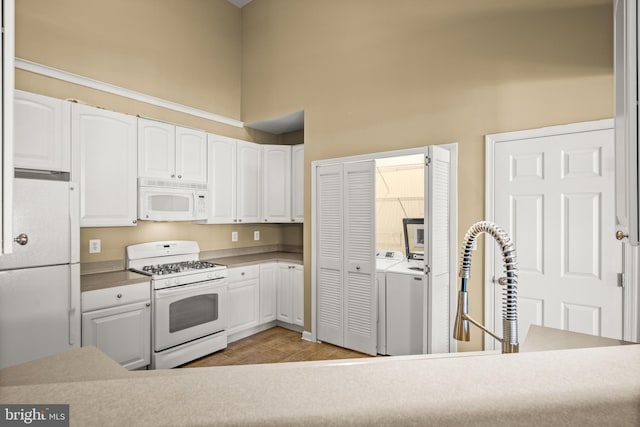 kitchen with independent washer and dryer, white cabinets, white appliances, and a towering ceiling