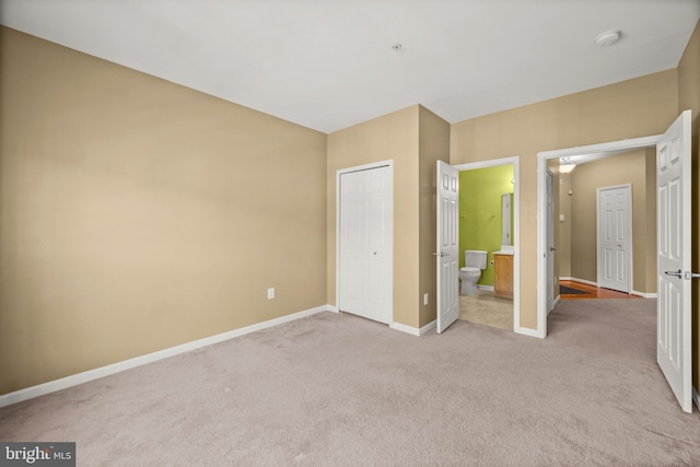 unfurnished bedroom with a closet, ensuite bathroom, and light carpet