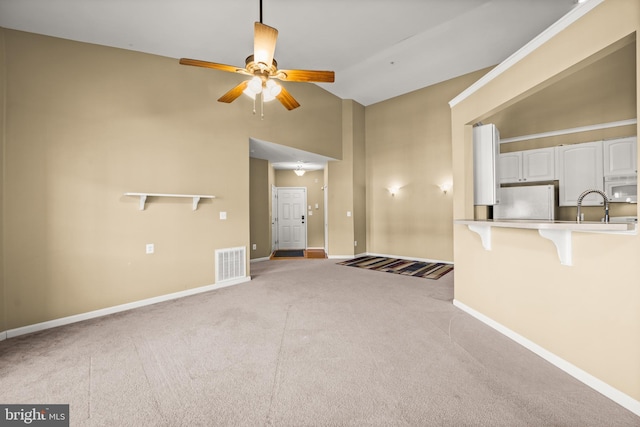 unfurnished living room with ceiling fan, light colored carpet, lofted ceiling, and sink