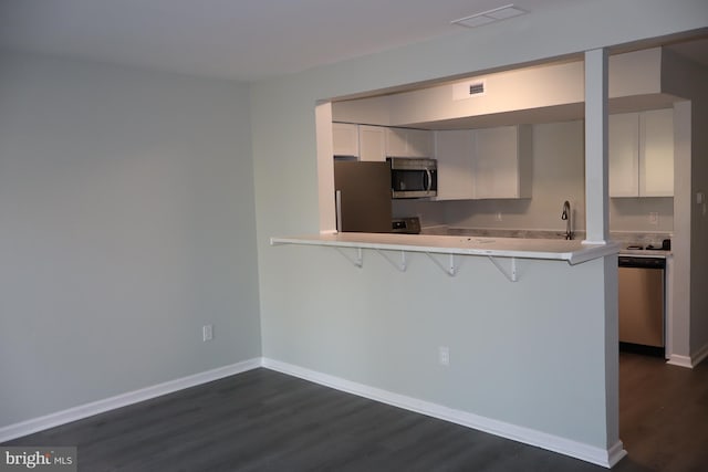 kitchen featuring white cabinetry, stainless steel appliances, dark hardwood / wood-style floors, a kitchen bar, and kitchen peninsula