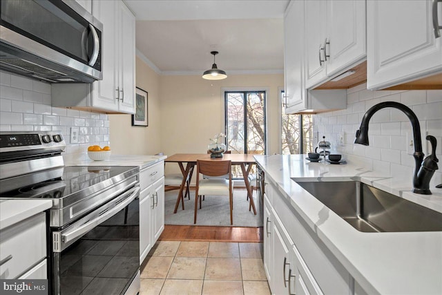 kitchen featuring white cabinetry, hanging light fixtures, sink, appliances with stainless steel finishes, and crown molding