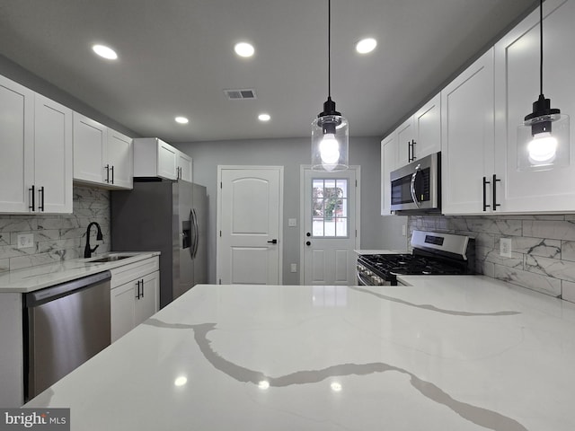 kitchen with pendant lighting, stainless steel appliances, light stone counters, and white cabinets