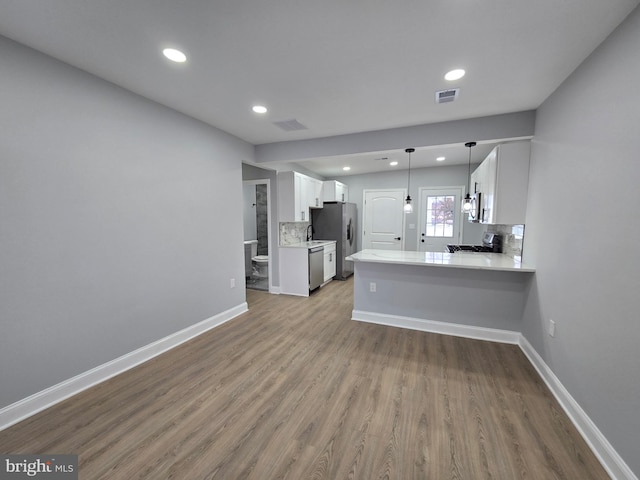 kitchen with pendant lighting, white cabinets, decorative backsplash, kitchen peninsula, and stainless steel appliances