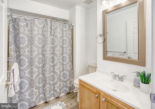 bathroom with toilet, vanity, wood finished floors, and visible vents