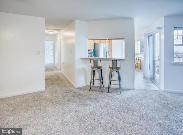 kitchen featuring light carpet, baseboards, a breakfast bar area, freestanding refrigerator, and a peninsula