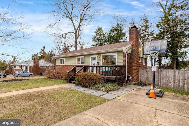 view of front of property with brick siding, fence, a wooden deck, a front lawn, and a chimney