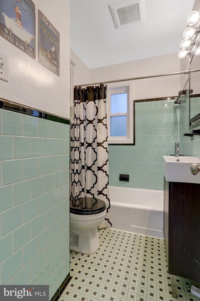 bathroom featuring tile walls, visible vents, shower / bathtub combination with curtain, toilet, and vanity