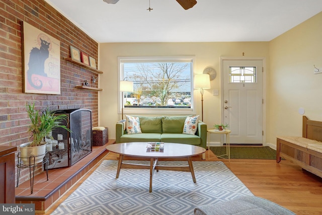 living room with a brick fireplace, a ceiling fan, baseboards, and wood finished floors