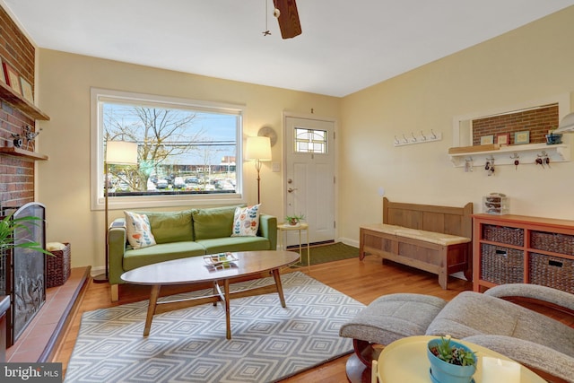 living room featuring baseboards, a brick fireplace, a ceiling fan, and light wood-style floors