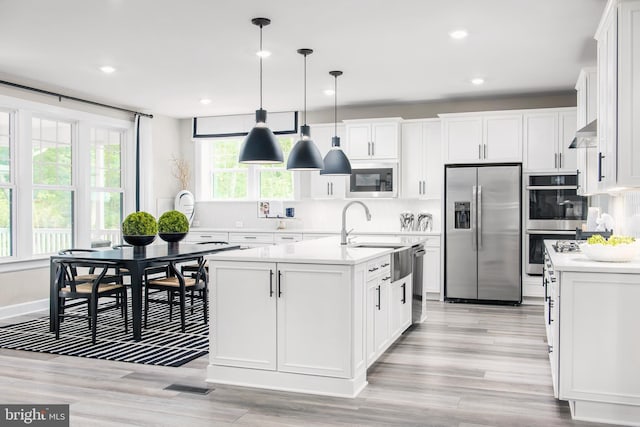 kitchen with pendant lighting, appliances with stainless steel finishes, an island with sink, and white cabinets