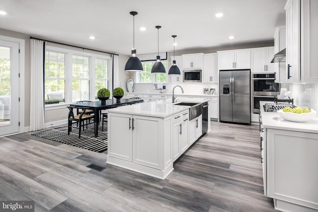 kitchen featuring ventilation hood, pendant lighting, stainless steel appliances, a kitchen island with sink, and white cabinets