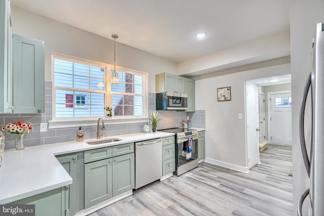 kitchen featuring sink, tasteful backsplash, light wood-type flooring, appliances with stainless steel finishes, and pendant lighting