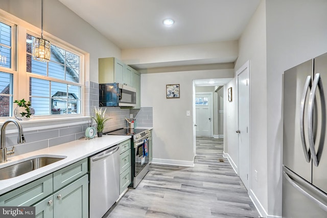 kitchen with sink, appliances with stainless steel finishes, pendant lighting, light hardwood / wood-style floors, and decorative backsplash