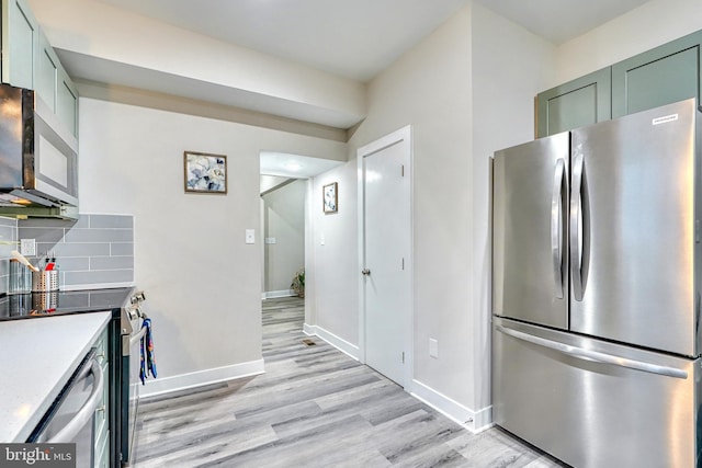 kitchen featuring appliances with stainless steel finishes, green cabinets, light hardwood / wood-style flooring, and backsplash