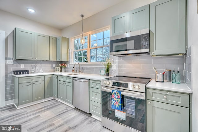 kitchen with sink, green cabinetry, stainless steel appliances, light hardwood / wood-style floors, and backsplash