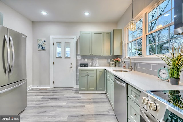 kitchen with sink, light hardwood / wood-style flooring, stainless steel appliances, tasteful backsplash, and decorative light fixtures