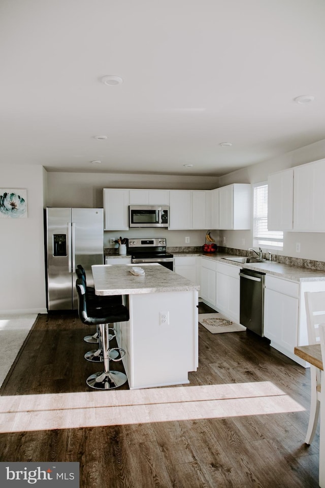 kitchen featuring sink, wood-type flooring, a kitchen island, stainless steel appliances, and white cabinets