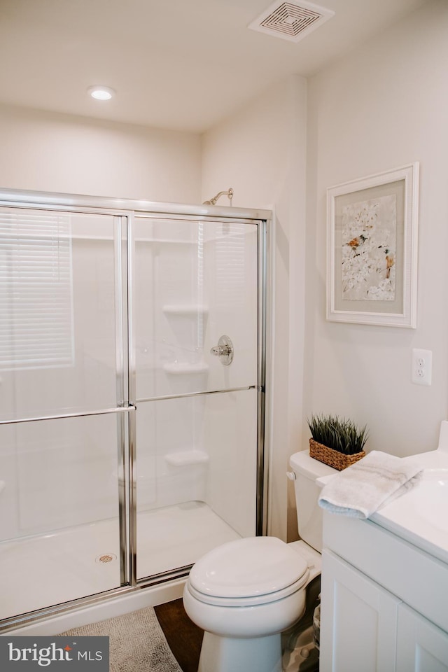 bathroom featuring vanity, a shower with shower door, and toilet