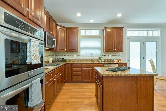 kitchen featuring a sink, light stone counters, appliances with stainless steel finishes, light wood finished floors, and decorative backsplash