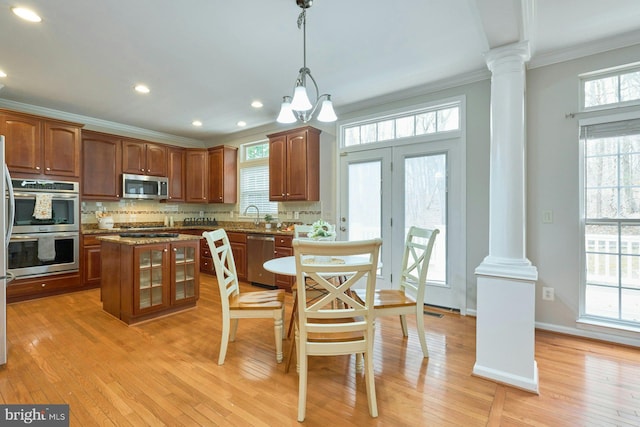 kitchen featuring light wood-type flooring, decorative columns, stainless steel appliances, crown molding, and decorative backsplash